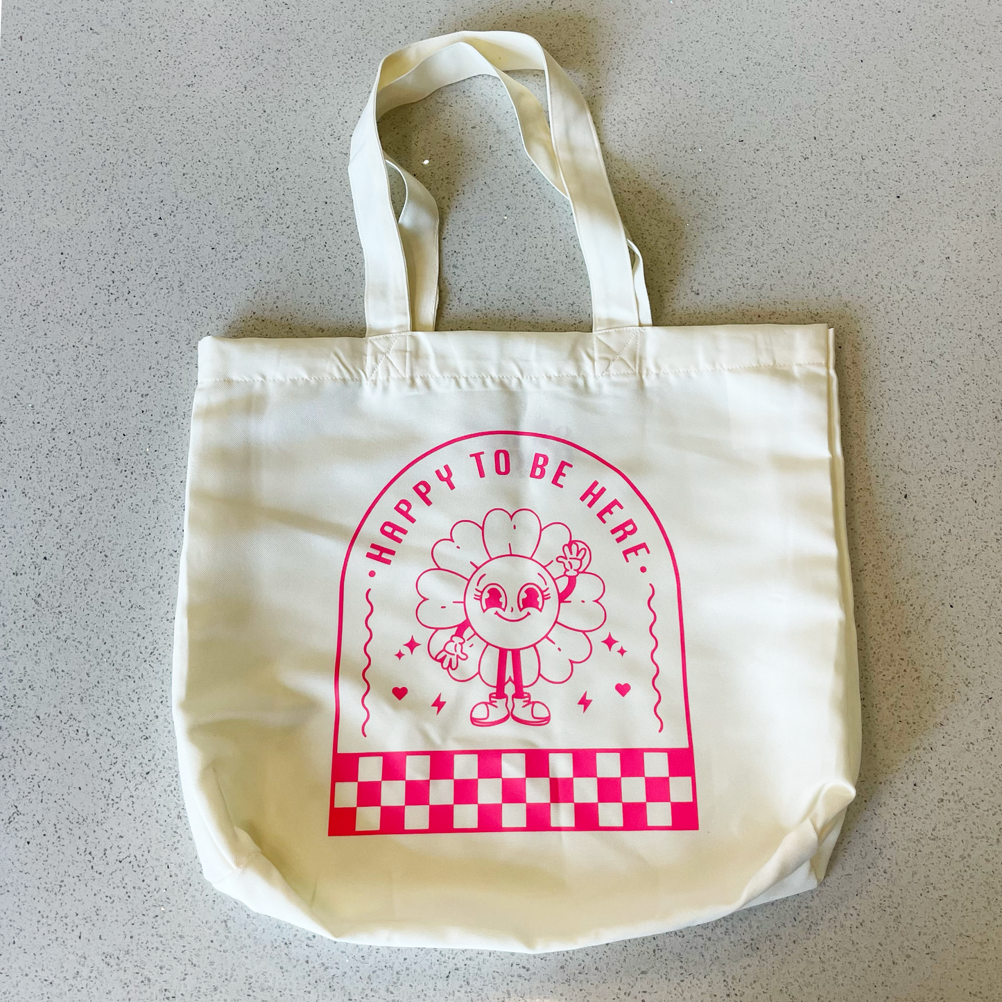 tote bag with design saying happy to be here with a happy flower waving in neon pink