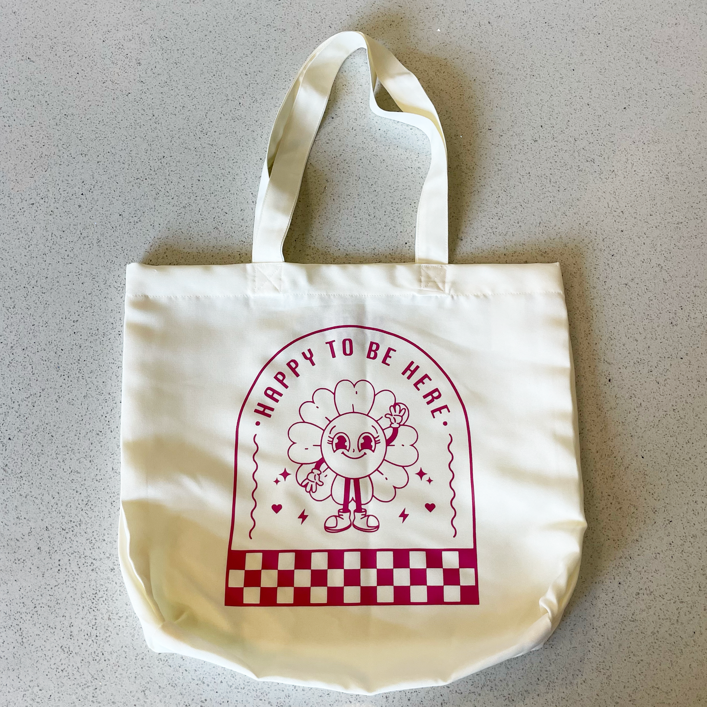 tote bag with design saying happy to be here with a happy flower waving in mauve