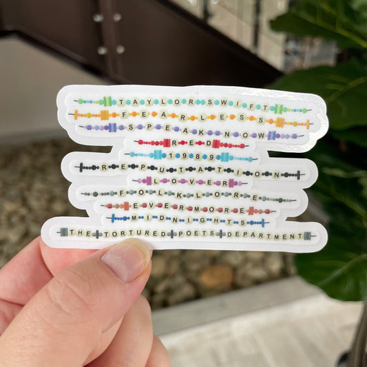 hand holding sticker that has all of taylor swifts albums as friendship bracelets on it