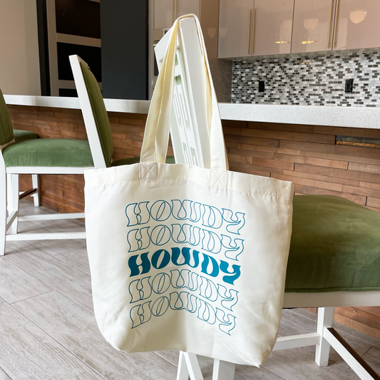 tote bag that says howdy in teal hanging from a chair